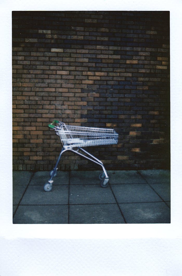 An isolated shopping cart stands against a textured brick wall backdrop.
