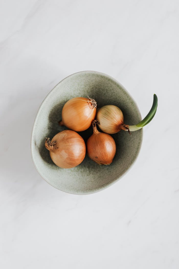 Top view of fresh whole onions in a ceramic bowl on a marble surface, perfect for culinary themes.